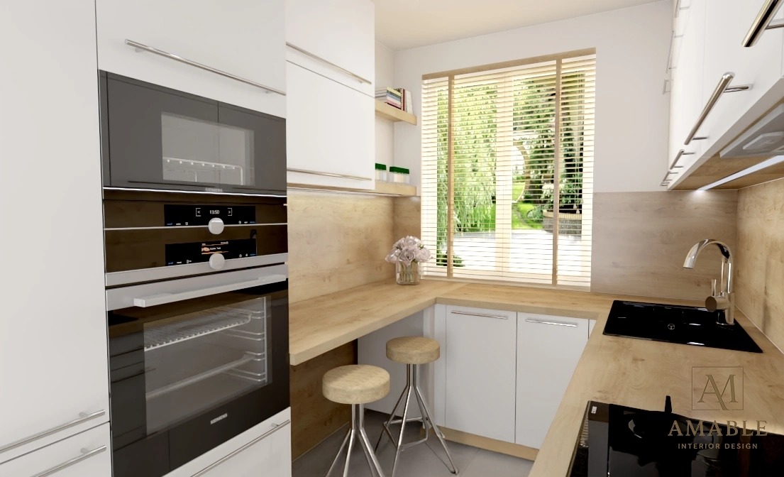 Jasna kuchnia z drewnianym blatem, stalowymi stołkami barowymi i dużym oknem z widokiem na zieleń. Nowoczesny piekarnik w zabudowie i subtelny bukiet kwiatów.