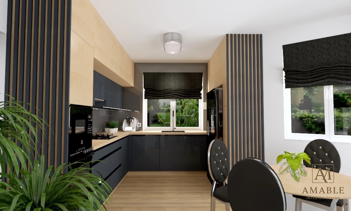 Nowoczesna kuchnia z szarymi szafkami, drewnianymi akcentami i dużym oknem z roletą rzymską. Na pierwszym planie stół z krzesłami i roślina doniczkowa.