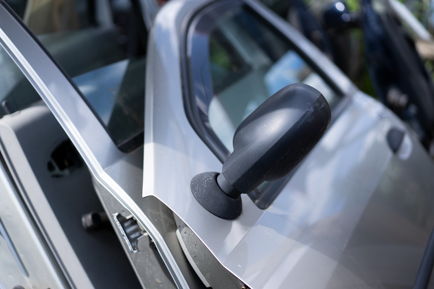 Fragment karoserii srebrnego samochodu z otwartymi drzwiami i lusterkiem bocznym, widoczne ślady użytkowania.