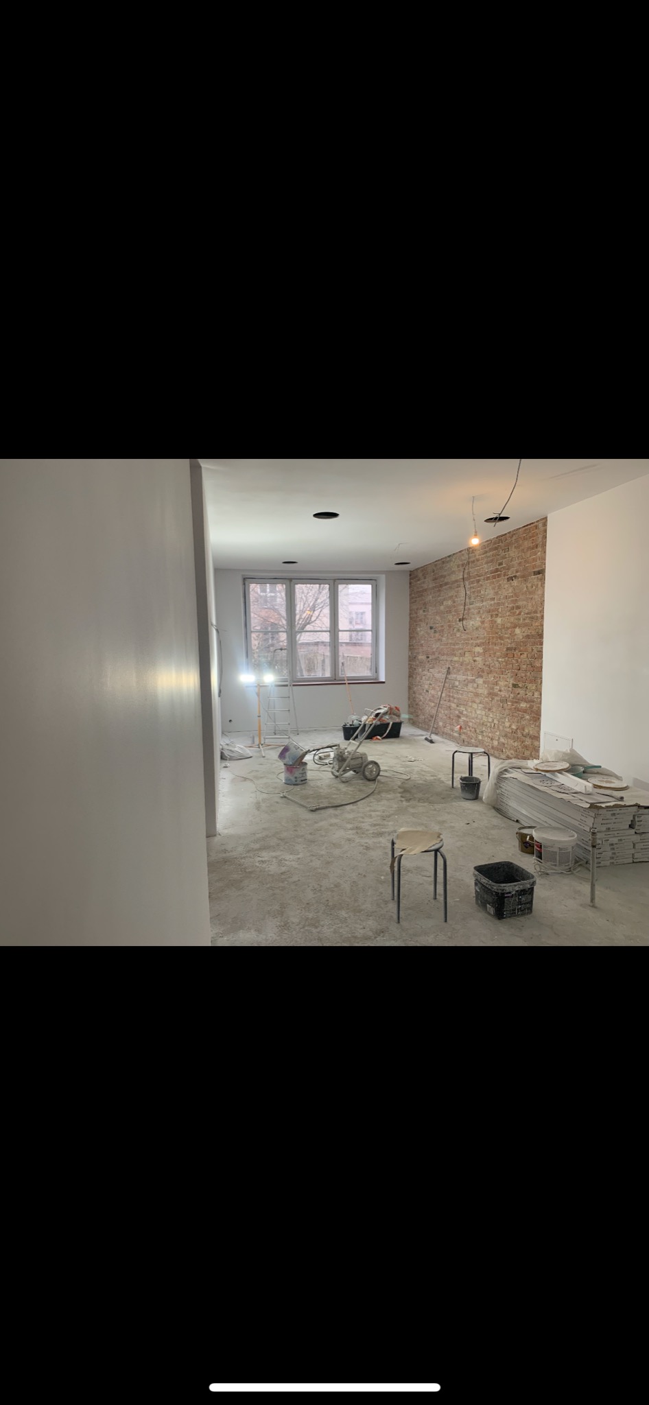 Wnętrze w trakcie prac remontowych we Włocławku: Częściowo pomalowane ściany, surowa cegła, sprzęt malarski, drabina i materiały budowlane.