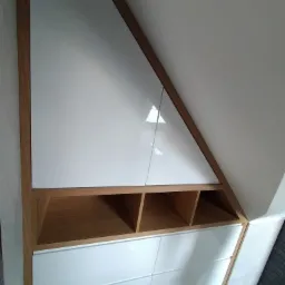 Szafa wnękowa na poddaszu z białymi frontami i drewnianym obramowaniem, widok z dołu.