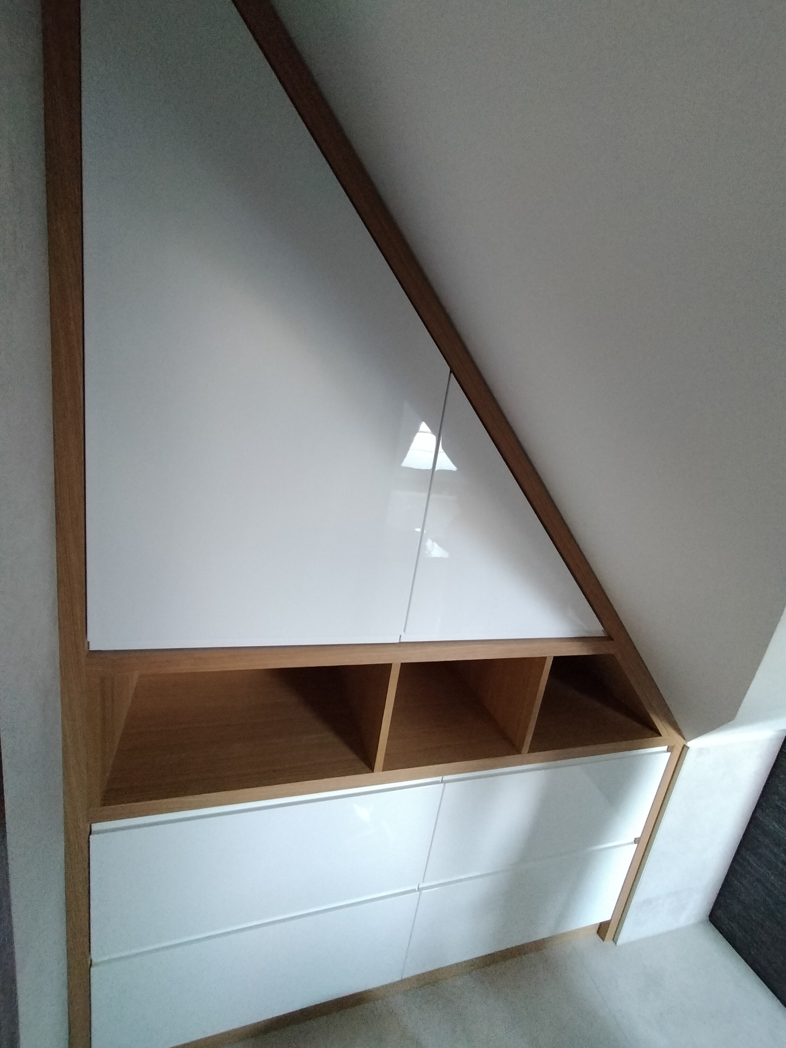 Szafa wnękowa na poddaszu z białymi frontami i drewnianym obramowaniem, widok z dołu.