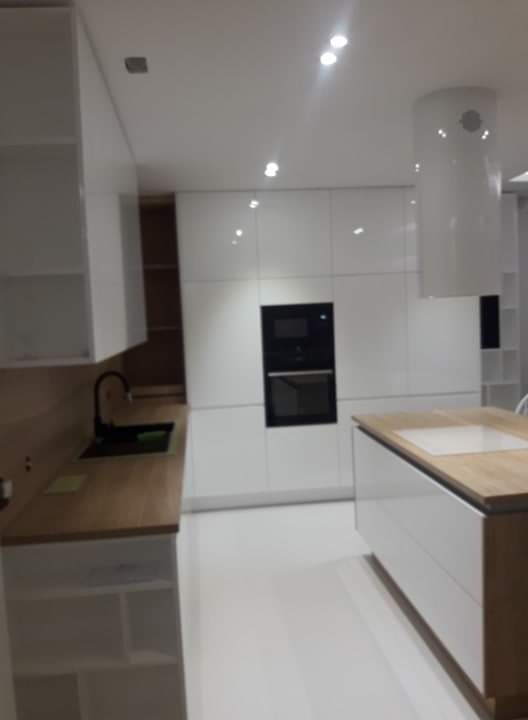 Nowoczesna kuchnia z białymi, lakierowanymi frontami, drewnianym blatem i czarną armaturą, oświetlona punktowymi lampami sufitowymi.