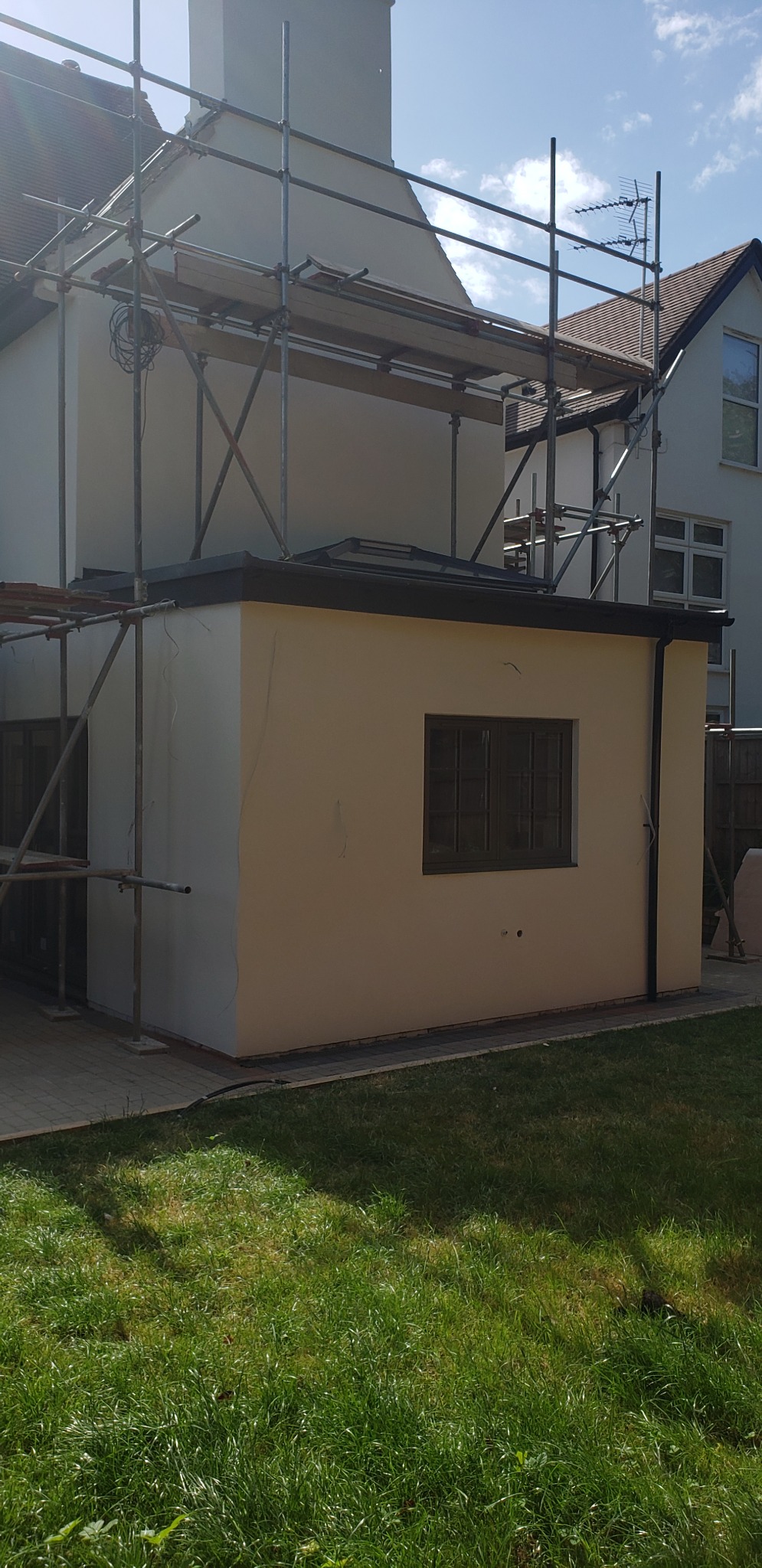 Nowo otynkowana elewacja rozbudowanej części domu z zamontowanym oknem, widoczne rusztowanie i trawnik.