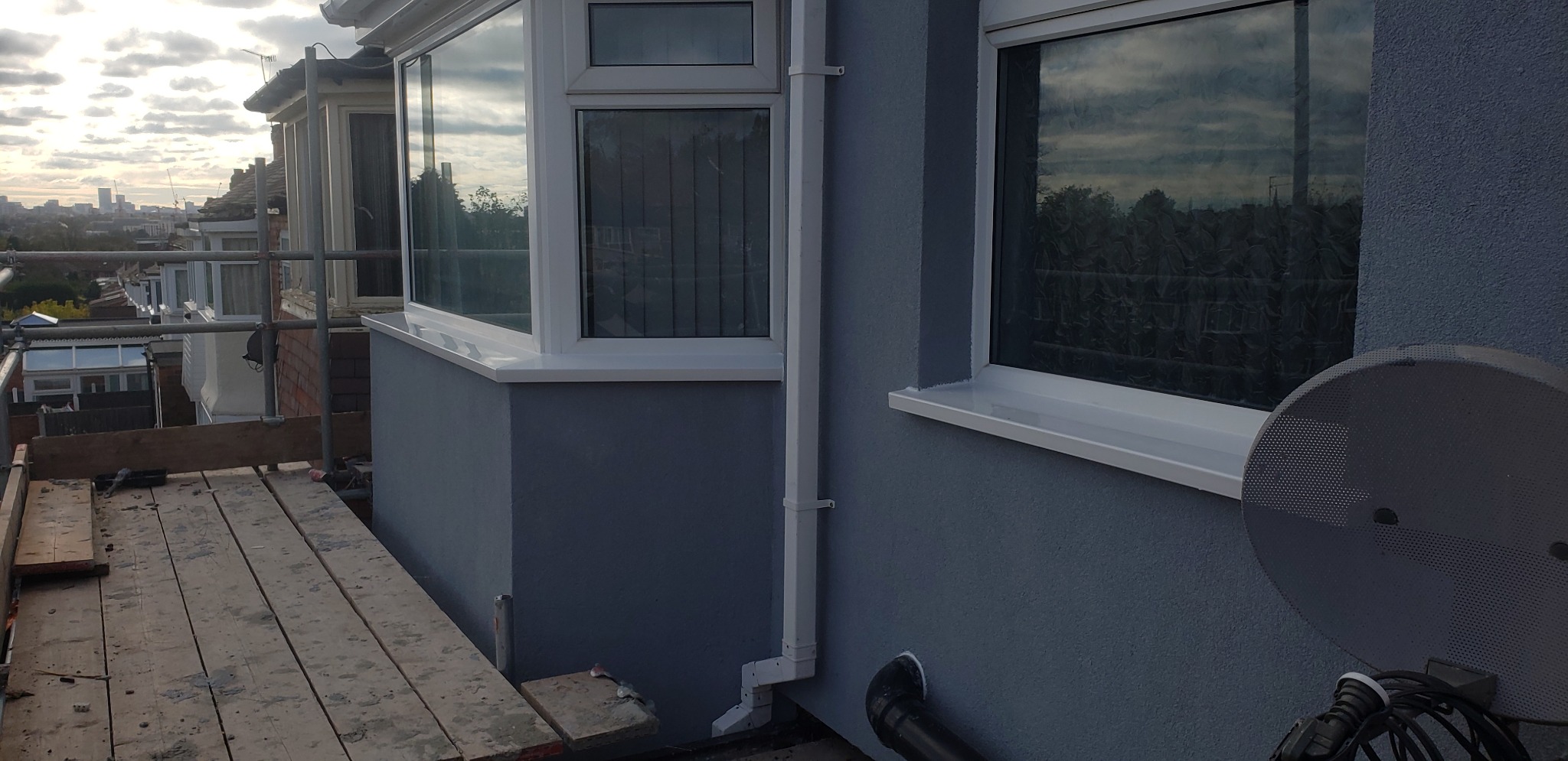 Świeżo otynkowana elewacja w odcieniach szarości z białymi obramowaniami okien, widok z rusztowania na tle panoramy miasta.