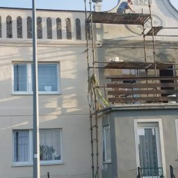 Magic Malarz - Pracownik na rusztowaniu odnawia elewację budynku z datą 1929, widoczne detale architektoniczne i elementy ozdobne.