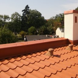 Magic Malarz - Pomarańczowa dachówka ceramiczna z kominem w tle, widok z góry na tle zieleni i błękitnego nieba.