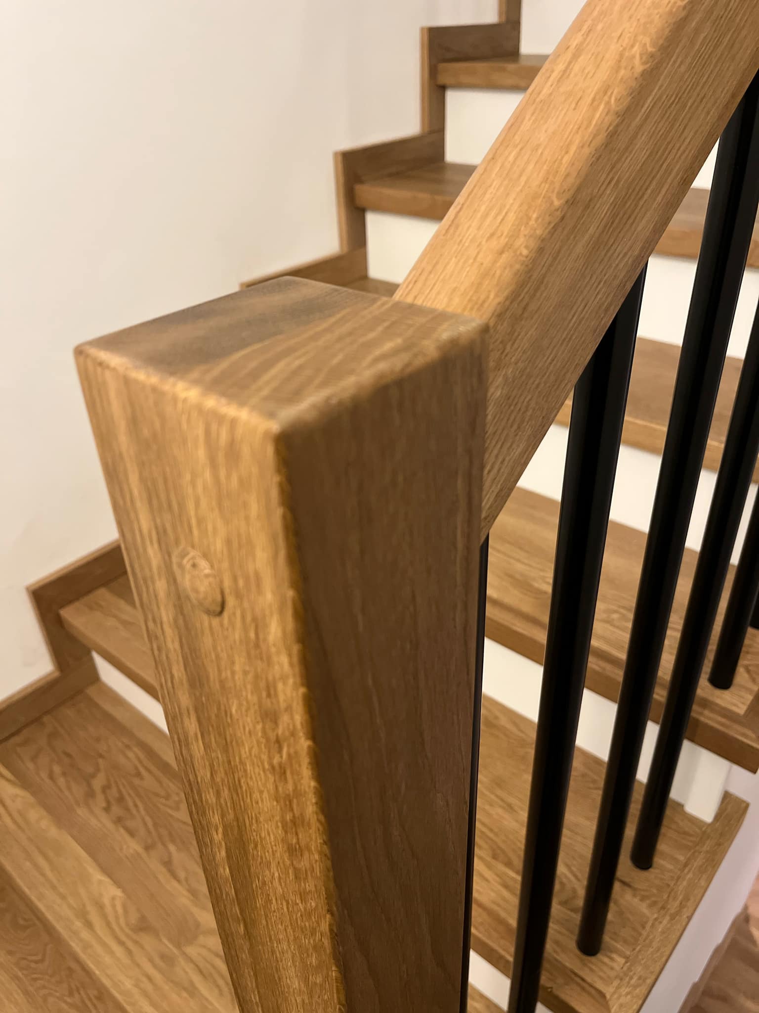Fragment drewnianych schodów z poręczą z czarnymi, pionowymi elementami i widocznym połączeniem elementów drewnianych na słupku.