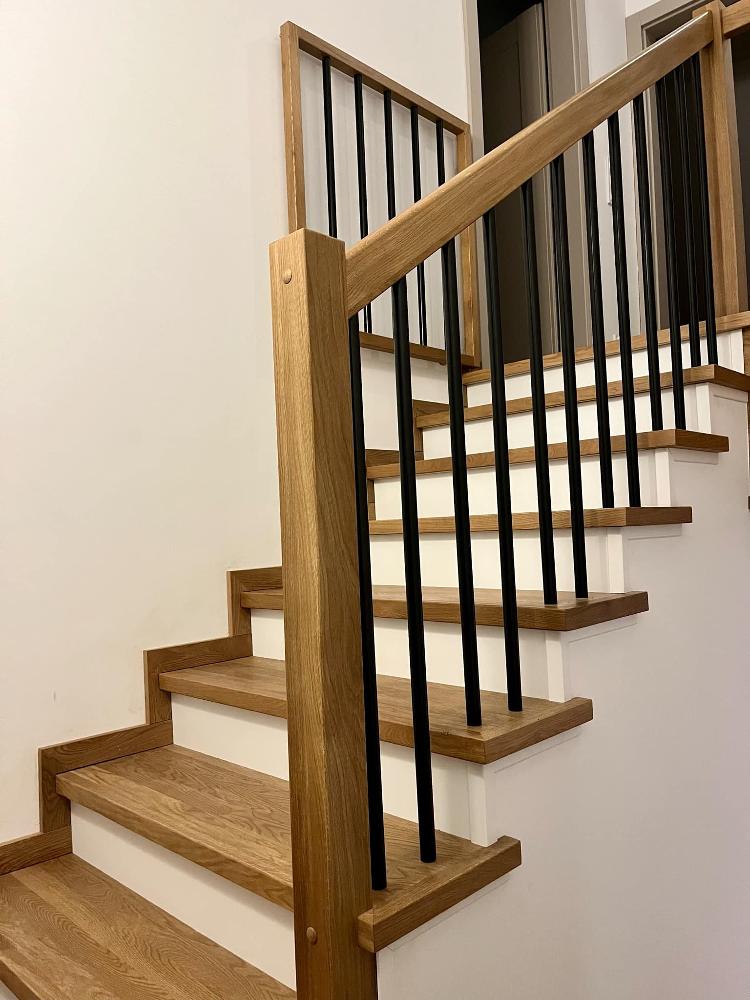 Nowoczesne schody z drewnianymi stopniami i czarnymi metalowymi balustradami, widok z dołu, minimalistyczny design.