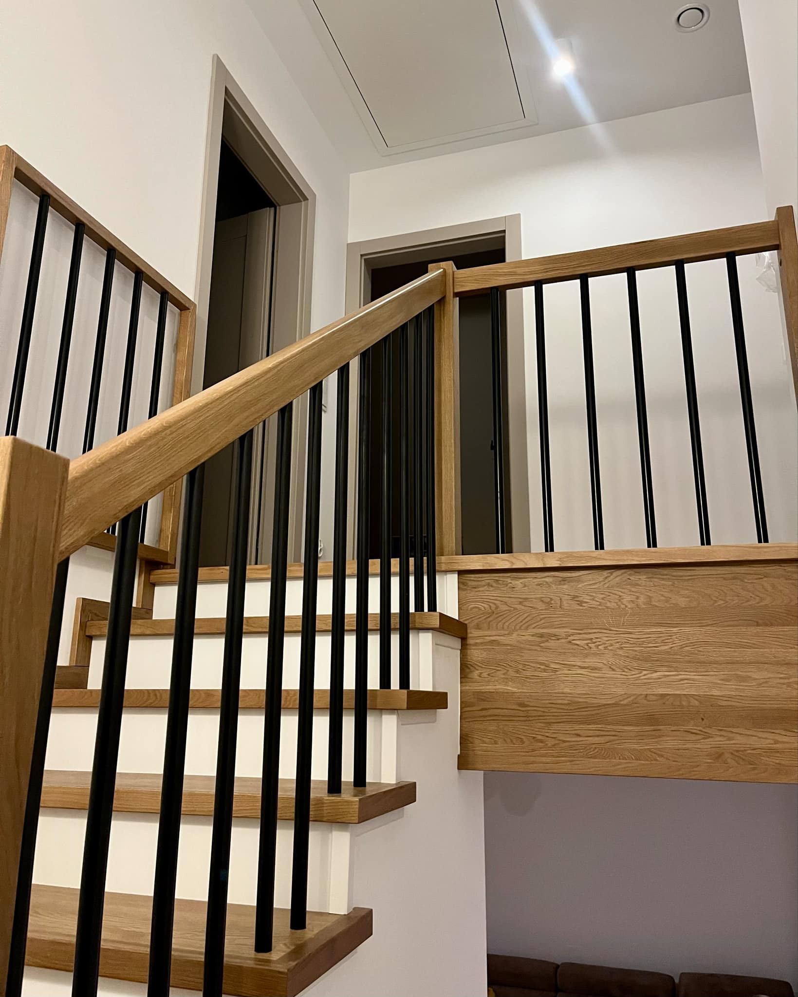 Nowoczesne schody z jasnego drewna z czarnymi balustradami w domu w Józefowie, widoczne drzwi w tle.