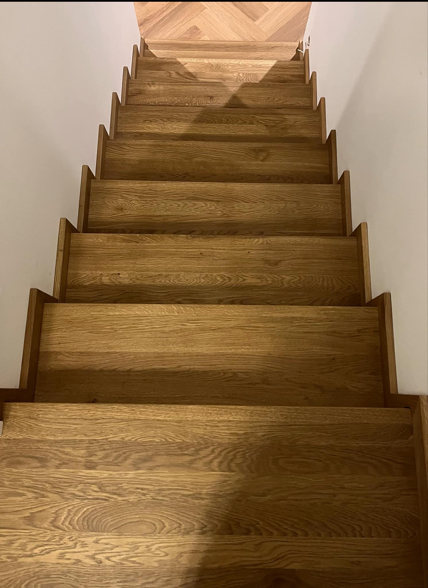 Drewniane schody z dębowymi stopniami, widok z góry, parkiet w jodełkę na podeście, białe ściany.