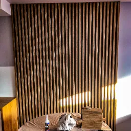 Montaż drewnianych lameli ściennych, widoczny klej montażowy, pędzel, ściereczka i zapasowe lamele na stole przykrytym folią ochronną.