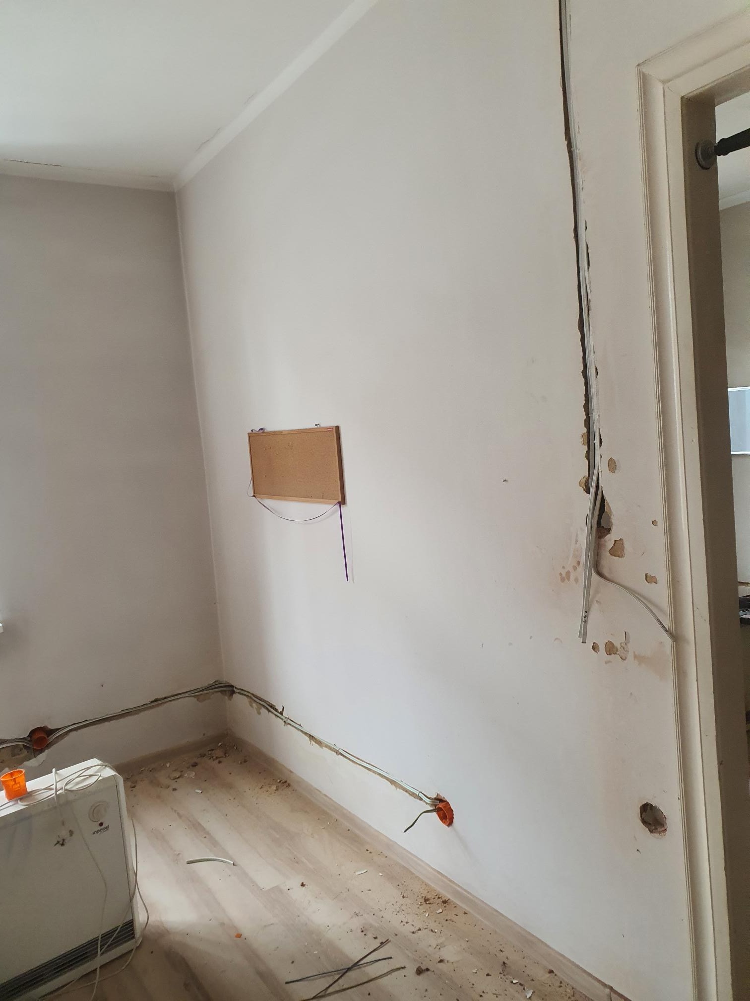 Pokój w trakcie remontu elektrycznego: widoczne przewody elektryczne prowadzone po ścianach, puszki instalacyjne, uszkodzona ściana przy futrynie i tymczasowy grzejnik elektryczny Inpool na podłodze.