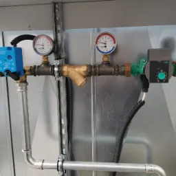 Fragment instalacji z manometrami, filtrem skośnym i pompą obiegową Wilo, zamontowanej na metalowej konstrukcji nośnej.