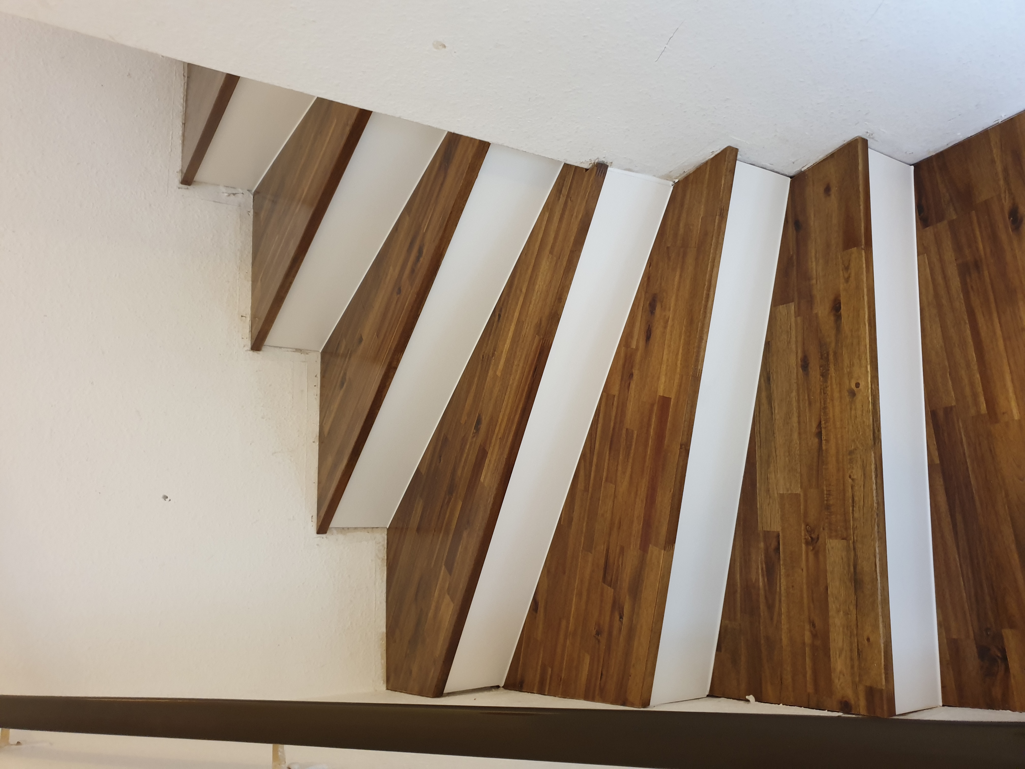 Nowoczesne schody z drewnianymi stopniami i białymi podstopnicami, widok z dołu, podkreślający minimalistyczny design i wykończenie wnętrza.