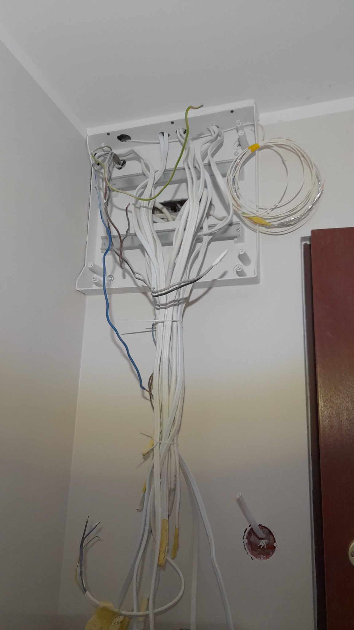 Rozdzielnica elektryczna z licznymi przewodami wychodzącymi na zewnątrz, część z nich związana opaską, widoczne także przewody wystające ze ściany, instalacja w trakcie prac.