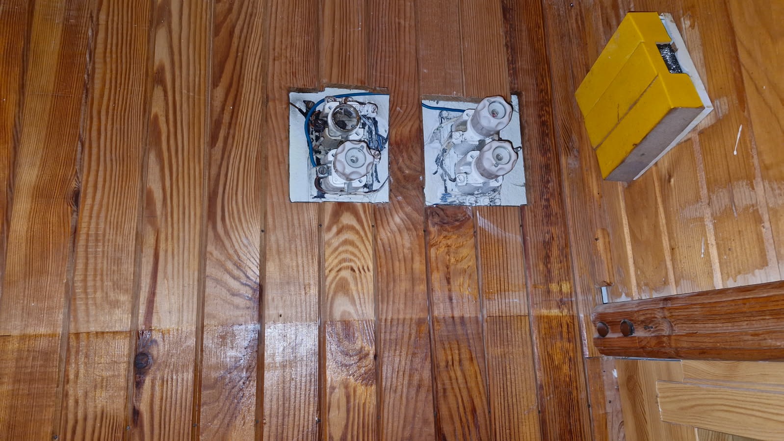 Stare, ceramiczne bezpieczniki topikowe zamontowane na drewnianej ścianie w Kobylnicy, widoczna instalacja elektryczna w stanie wymagającym interwencji.