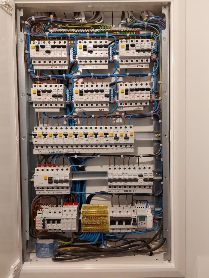Rozdzielnica elektryczna z zabezpieczeniami nadprądowymi i różnicowoprądowymi marki Eaton, uporządkowane okablowanie w kolorach, widoczne listwy zaciskowe i elementy sterujące.