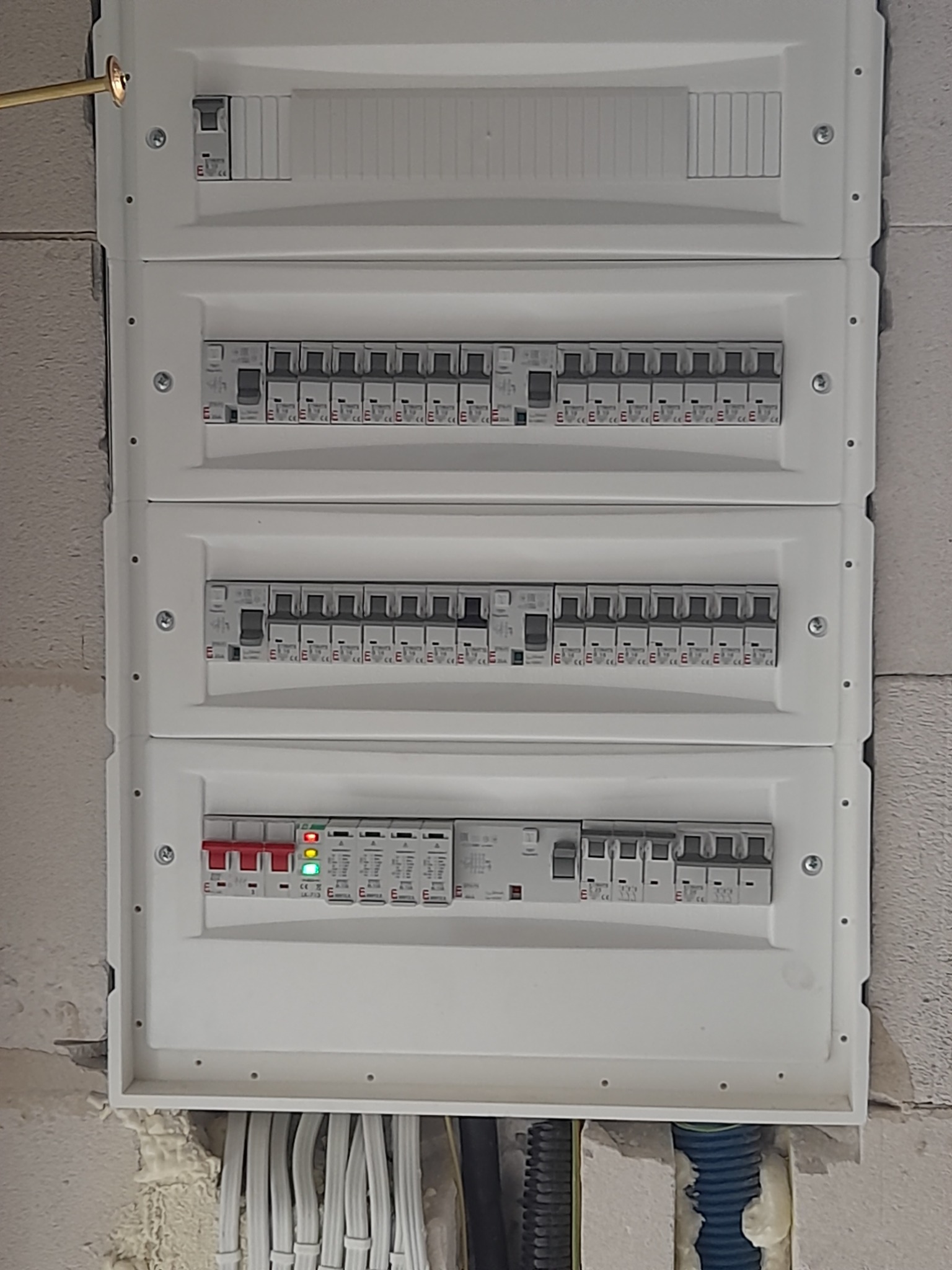 Rozdzielnica elektryczna z wieloma bezpiecznikami, widoczne kable wchodzące do skrzynki, zamontowana na surowej ścianie.