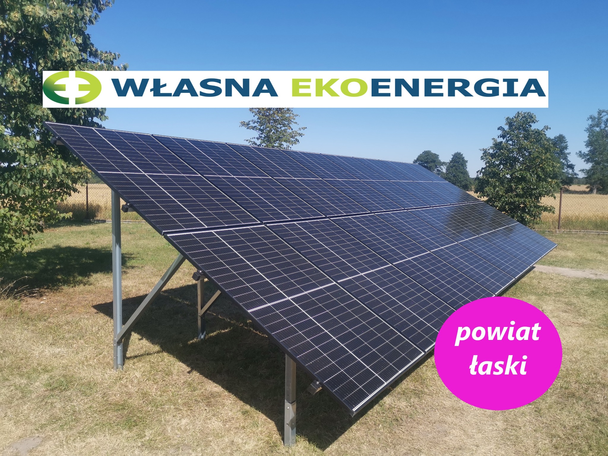 Instalacja paneli słonecznych na metalowej konstrukcji na trawiastym terenie, z logo firmy 'Własna Ekoenergia' i oznaczeniem 'powiat łaski' nałożonym graficznie.