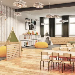 Jasne, przestronne wnętrze sali zabaw z drewnianą podłogą, stolikami dla dzieci, tipi, pufami w kształcie gruszek i dekoracjami ściennymi z motywem drzew.