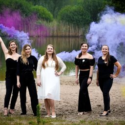 Fotografia Katarzyna Guzicka - Grupa pięciu kobiet pozuje na piaszczystej plaży z kolorowymi dymami w tle, jedna z nich trzyma dymiącą świecę w uniesionej ręce.