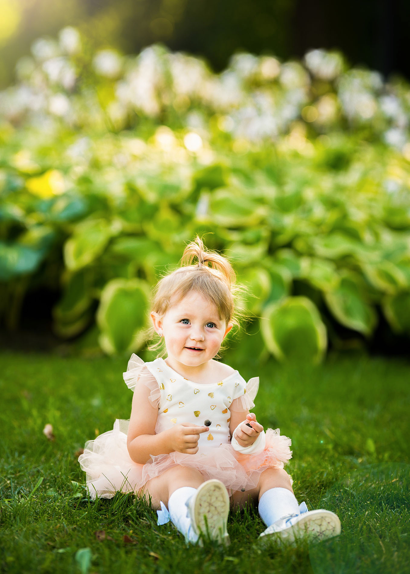 Uśmiechnięta dziewczynka w tiulowej spódniczce siedzi na trawie, trzymając jagodę, z rozmyte tło z zieleni.