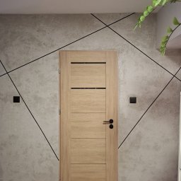 DANMONT Daniel Wilk - Wnętrze z drewnianymi drzwiami na tle ściany z szarą strukturą betonu i czarnymi, geometrycznymi liniami. Widoczny fragment rośliny doniczkowej i włączniki światła.