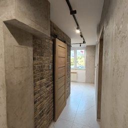 DANMONT Daniel Wilk - Korytarz w stylu loft: cegła dekoracyjna, betonowe tynki, drewniane drzwi przesuwne, oświetlenie szynowe i marmuropodobna posadzka. Widok z perspektywy.