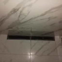 Ściana łazienki wyłożona białymi płytkami imitującymi marmur z widocznym odpływem liniowym w podłodze.