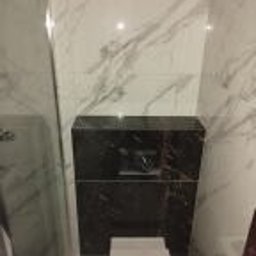 Wykończmy To - Obudowa stelaża podtynkowego WC wykończona czarnym marmurem z białymi żyłami, na tle białych płytek imitujących marmur. Widoczny fragment miski WC.