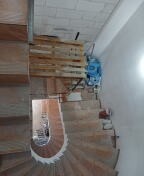 Wnętrze w trakcie remontu: drewniane schody spiralne na etapie wykończenia, zabezpieczone drewnianą konstrukcją, ściany częściowo wykończone, widoczne worki z materiałami budowlanymi.