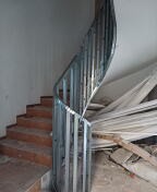 Konstrukcja schodów spiralnych wykonana z metalowych profili, przygotowana do obłożenia płytami, widoczne stopnie schodów i elementy składowane w tle.