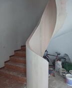 Surowe drewniane schody z falistą ścianką działową z płyty, widoczne ślady prac wykończeniowych, rower oparty o ścianę w tle.