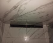 Ściana łazienki wyłożona białymi płytkami imitującymi marmur z widocznym odpływem liniowym w podłodze.