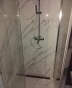 Kabina prysznicowa z białymi płytkami imitującymi marmur, widoczna armatura i przesuwne drzwi z metalowymi ramami.