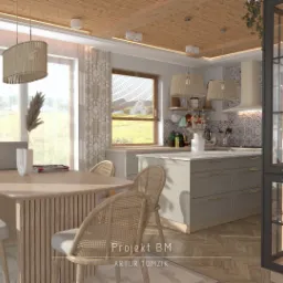 Wnętrze kuchni z jadalnią w stylu boho, drewniany stół z rattanowymi krzesłami, wyspa kuchenna w kolorze szarym, przeszklona witryna z dekoracjami, widok na zielony krajobraz za oknem.