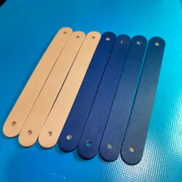 Paski skórzane: trzy w odcieniach beżu i cztery w różnych odcieniach niebieskiego, wszystkie z otworem na jednym końcu, leżące na niebieskim tle.