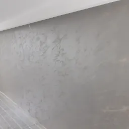 Ściana wewnętrzna z dekoracyjnym, szarym tynkiem imitującym beton, świeżo położona instalacja ogrzewania podłogowego, widoczny kabel zasilający.