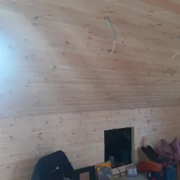 Poddasze wykończone boazerią z widocznymi przewodami elektrycznymi, otworem rewizyjnym i narzędziami pracy.