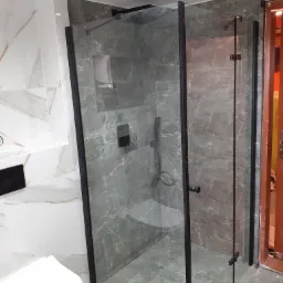 Nowoczesna kabina prysznicowa z czarnymi profilami i marmurowymi płytkami, widok na toaletę i fragment drzwi wejściowych.