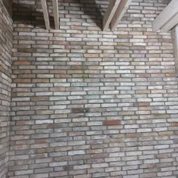 Wnętrze w trakcie budowy z widoczną ścianą z cegły klinkierowej w odcieniach beżu i brązu oraz elementami drewnianej konstrukcji stropu.