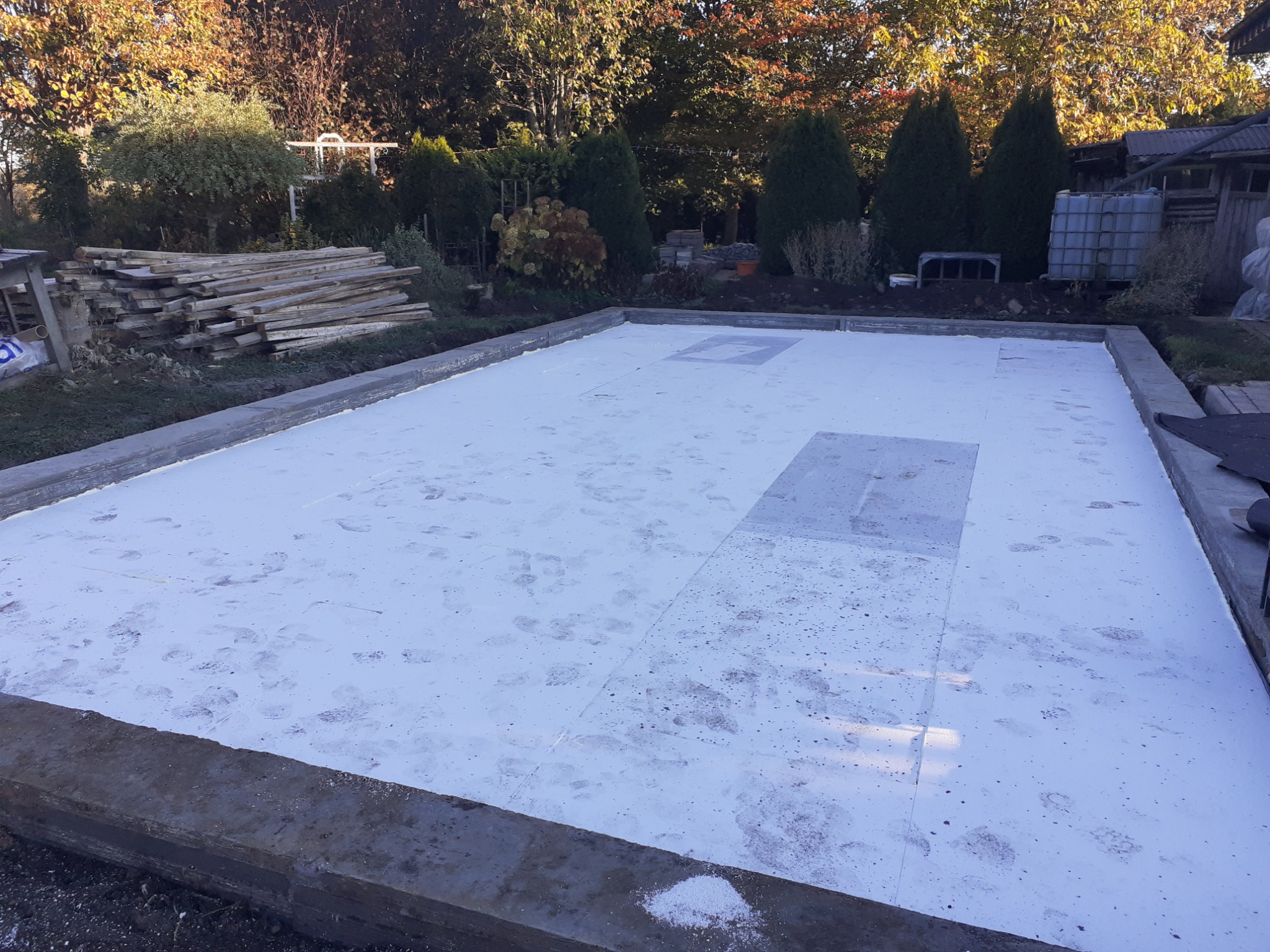 Przygotowany fundament pod budynek, z widoczną izolacją termiczną w postaci białych płyt styropianowych, zabezpieczonych betonową wylewką obwodową. Widoczne odciski butów na izolacji.