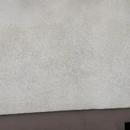 Fragment elewacji z widoczną różnicą w czystości po lewej i prawej stronie, obok rynna spustowa, ciemna podmurówka i otwór wentylacyjny.