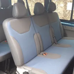 Wnętrze niebieskiego busa z widocznymi dwoma rzędami foteli w odcieniach szarości i błękitu, z otwartymi drzwiami bocznymi.