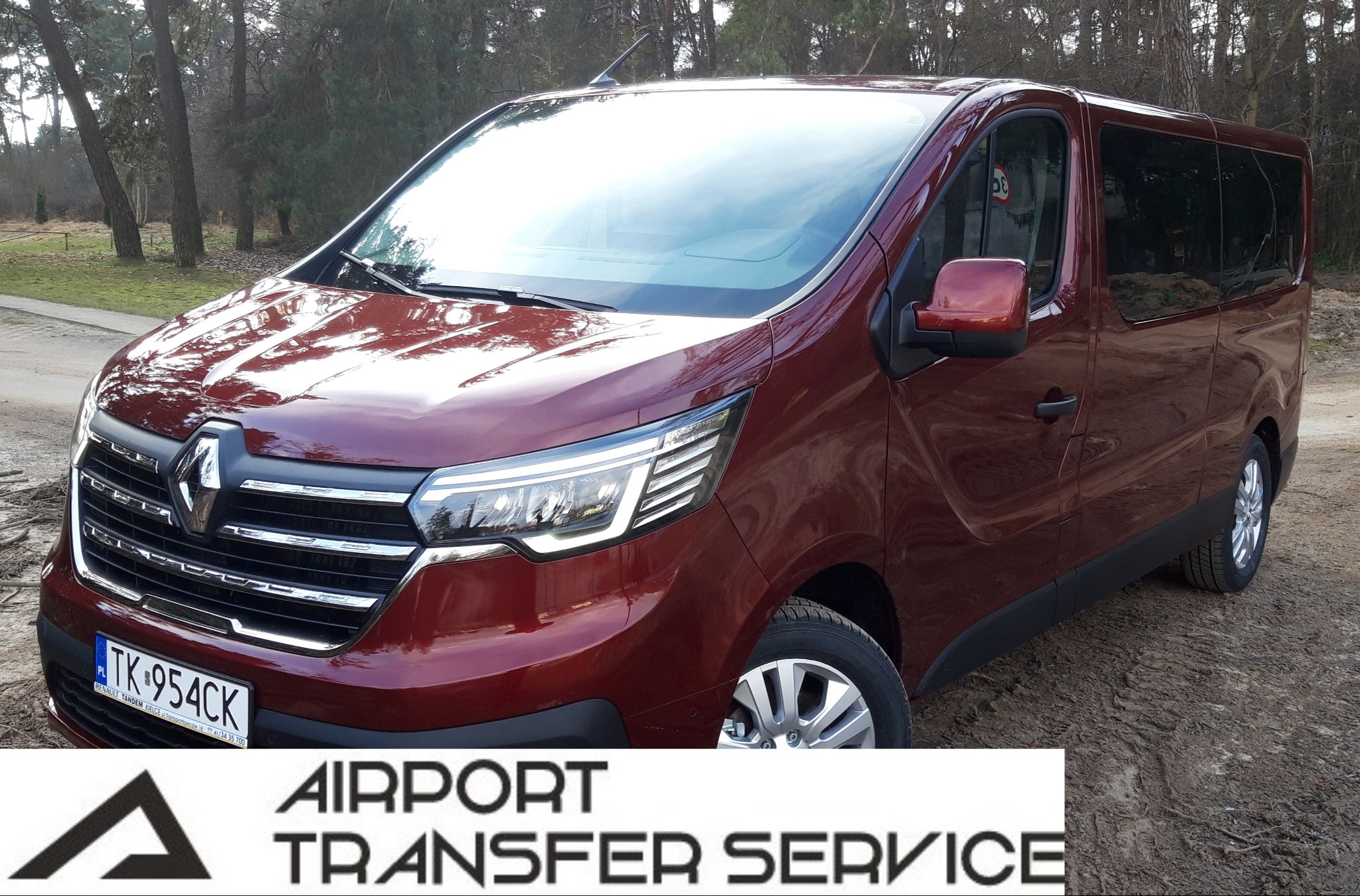 Bordowy Renault Trafic z polską rejestracją TK-954CK, zaparkowany na ziemistej nawierzchni, z logo 'Airport Transfer Service' w dolnej części kadru.