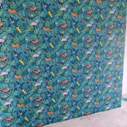 Ściana pokryta tapetą w tropikalny wzór z motywami zwierzęcymi: tygrysy, flamingi i ptaki, w odcieniach zieleni i niebieskiego, z fragmentami niezabezpieczonej podłogi w dolnej części kadru.