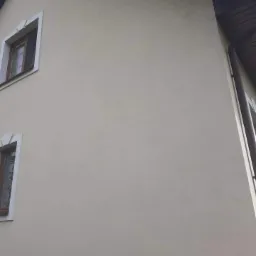 Odnowiona elewacja domu jednorodzinnego w odcieniach beżu po wykonanych pracach, widoczne dwa okna z drewnianymi ramami i system rynnowy. Na zdjęciu widnieją emotikony 'OK' oraz 'kciuk w górę'.