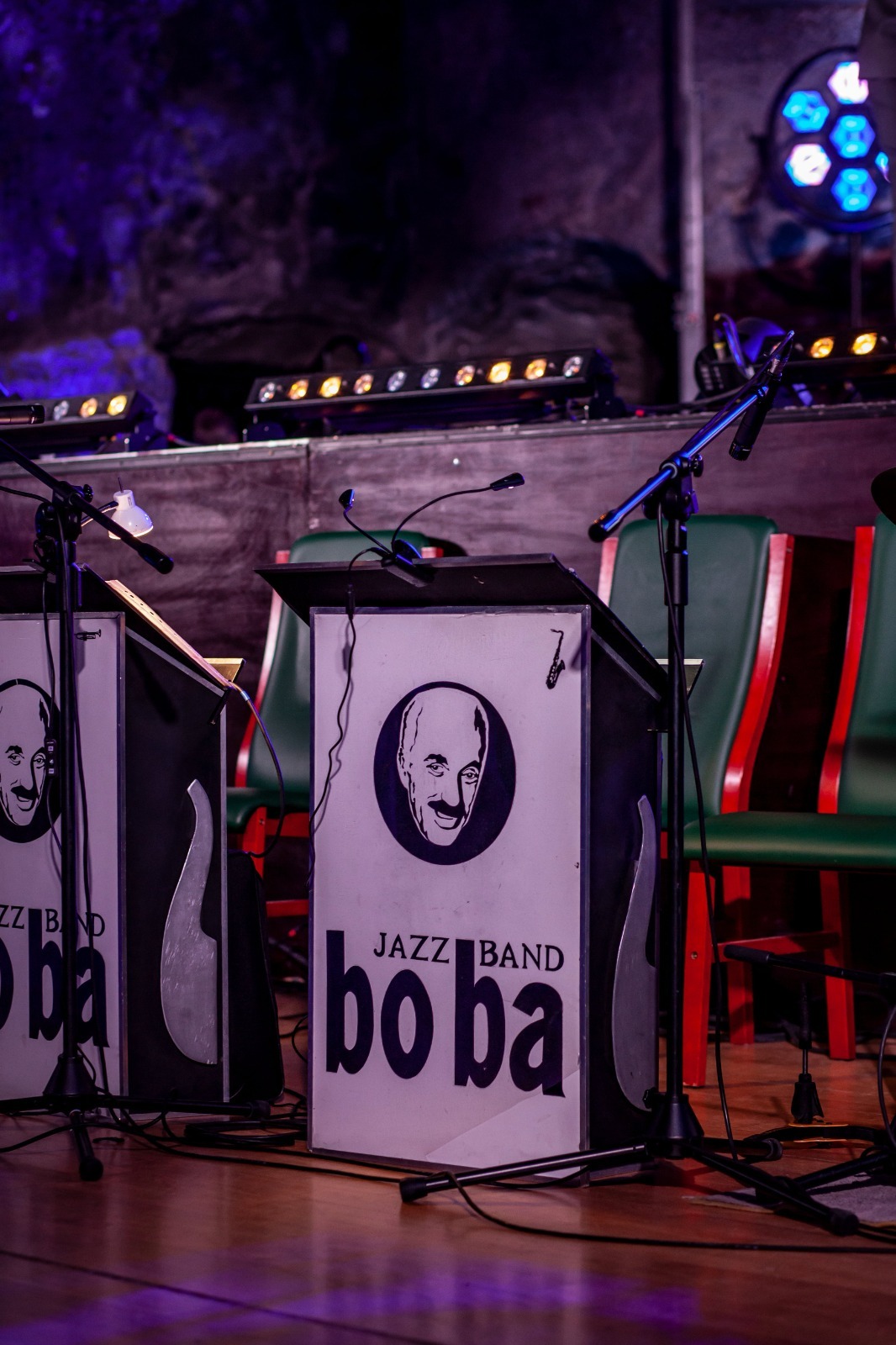 Scena z podświetlonymi pulpitami dla muzyków jazzowych z logo zespołu 'bo ba', mikrofonami i krzesłami w tle, tworząca unikalny klimat koncertu.