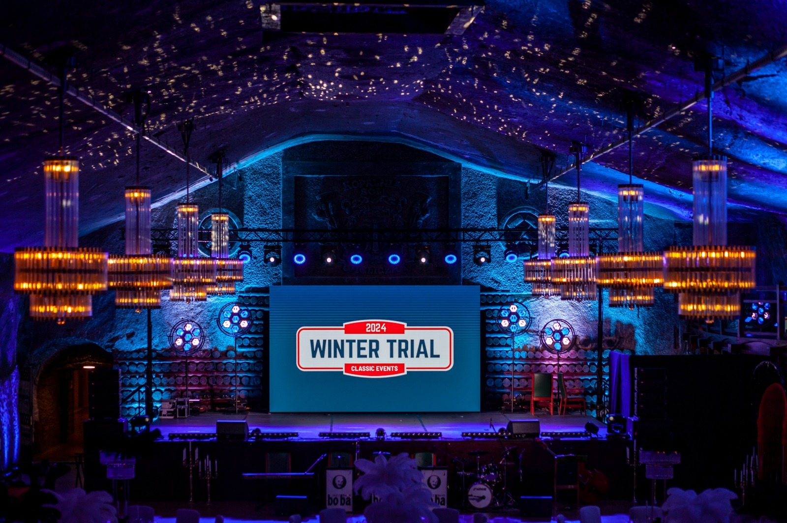 Scena eventowa w grocie solnej z oświetleniem, ekranem LED z napisem 'Winter Trial' i dekoracjami. Unikalne oświetlenie i surowy charakter wnętrza.